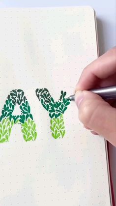 someone is drawing the letters in green leaves on a notepad with a marker pen