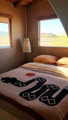 a bed in a room with two windows and a rug on the floor next to it