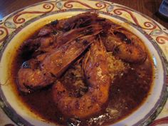 a plate full of shrimp and rice with sauce on the side, next to a bottle of wine