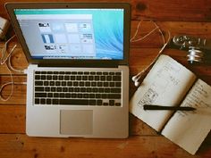 an open laptop computer sitting on top of a wooden table next to a notebook and camera