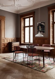 a dining room table and chairs in front of two large windows with wooden paneling