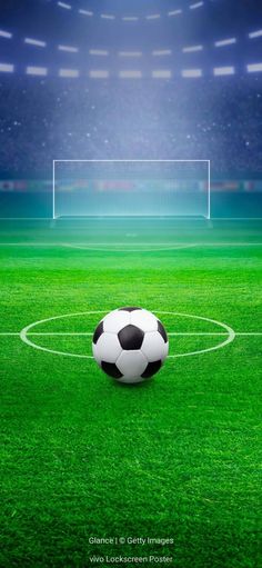 a soccer ball sitting on top of a lush green field in front of a stadium