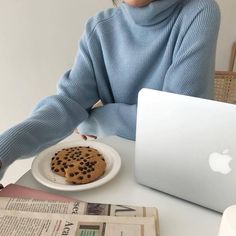 a woman sitting at a table with a plate of cookies in front of her laptop