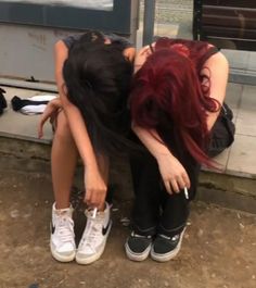 two young women sitting on the ground with their heads touching each other's hands