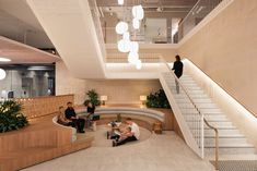 three people sitting on benches in the middle of a lobby with stairs and planters