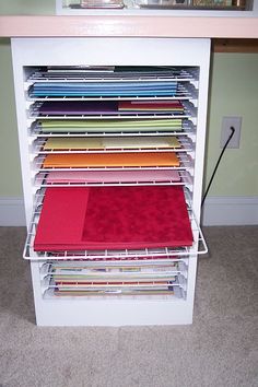 a white shelf filled with lots of different colored fabrics on top of carpeted flooring