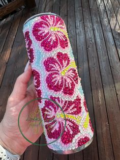 a hand holding a pink and yellow flowered can cooler with the lid down on a wooden deck