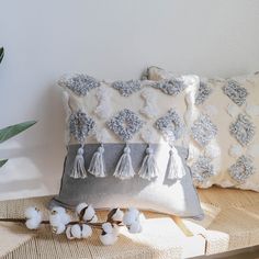 two decorative pillows sitting next to each other on a table with cotton balls and plants