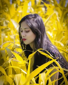 a woman with long hair standing in the middle of some yellow leaves and looking down at her face