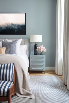 a bed room with a neatly made bed next to a painting on the wall and a dresser