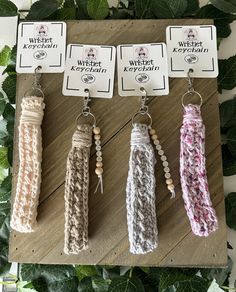 four keychains with different colors and designs hanging from hooks on a wooden board