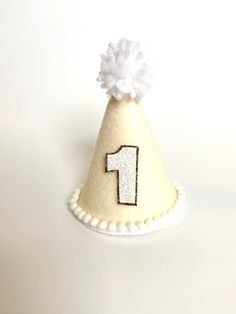 "These MINI party hats are the perfect accessory for your little one's big day or photo session. All hats are made to order. Each hat along with the bows and embellishments are carefully handcrafted so each hat is unique and will vary slightly because of this.  PLEASE LEAVE YOUR EVENT DATE AT CHECKOUT. PARTY HAT FEATURES: -Mini Party Hat (approximately 3\"x5\")  -Ivory/linen felt-covered hat designed with a custom template -White glitter number with white border or gold glitter border (of your c Pastel Cake Smash, Mini Birthday Cake, Mini Pinscher, Daisy Party, Twins 1st Birthdays, Hat Headband, Mini Cakes Birthday, Winter Wonderland Party, Yarn Pom Pom