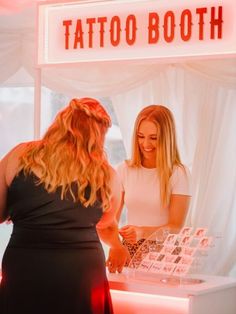 two women standing in front of a tattoo booth