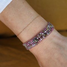 a woman's hand with a beaded bracelet on her left wrist and a gold chain