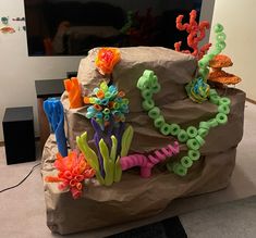 a rock covered in fake sea life sits on the floor next to a flat screen tv