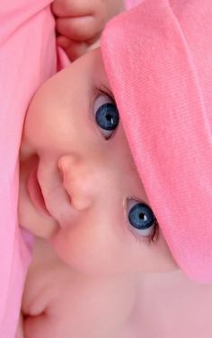 a close up of a baby with blue eyes and a pink blanket on its head