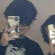 two young men taking pictures with their cell phones in front of the mirror, one holding his phone up to his face