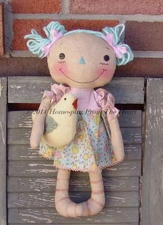 a stuffed doll is holding a bird on the back of a wooden bench with a brick wall in the background