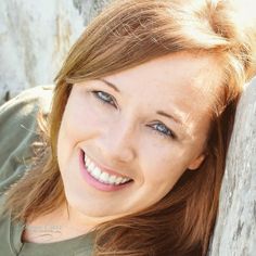 a smiling woman leaning against a rock wall