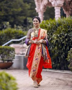 a woman in an orange and red sari walks down the street with her hand on her hip