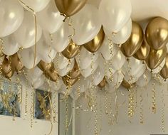 gold and white balloons are hanging from the ceiling