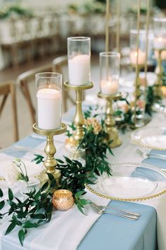 the table is set with candles, plates and greenery for an elegant wedding reception