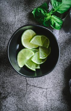 limes in a black bowl with basil on the side