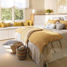 a large bed sitting in a bedroom next to a window filled with yellow and white pillows