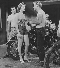 black and white photograph of people standing around motorcycles