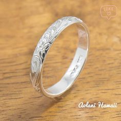 a wedding ring with an engraved design on the front and side, sitting on a wooden surface