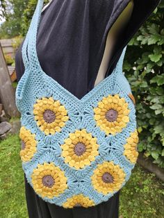 a crocheted bag with sunflowers on the front and bottom, hanging from a mannequin's dummy