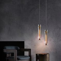 two lights hanging from the ceiling above a table and chair in front of a gray wall