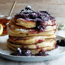 a stack of pancakes covered in blueberries and syrup