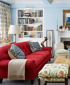 a red couch sitting in front of a fireplace next to a white chair and ottoman