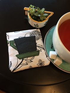 a cup of tea sits next to a potted plant on a black table top