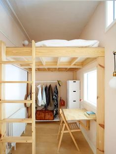 a loft bed with a desk underneath it and clothes hanging on the wall behind it