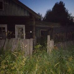 an old wooden house sitting in the middle of tall grass at night with no one around it