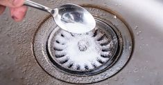 a person is holding a spoon over a sink drain with water running down the drain