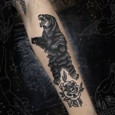 a black and white bear tattoo on the left arm with roses around it, sitting on top of a man's leg