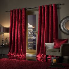 a living room with red curtains and a chair in front of a window overlooking the city