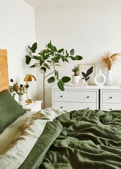 a bed with green sheets and pillows next to a potted plant on the nightstand