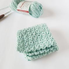 a crochet dishcloth and knitting needles on a white surface with yarn in the background