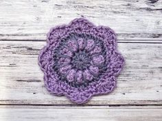 a purple crocheted flower sitting on top of a wooden table