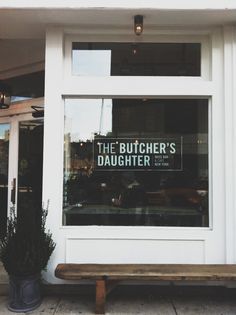 the butcher's daughter sign is displayed in the window behind a wooden bench and potted plant