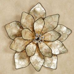 a metal flower on a beige wall with white and silver petals in the shape of a flower