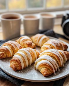 croissants with icing on a plate next to two cups of coffee