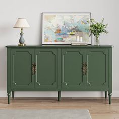 a green sideboard with three doors and two lamps on it in front of a white wall