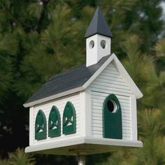 a small white church with a black roof and green trim around the steeple is shown in front of some trees