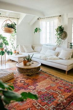 a living room filled with lots of furniture and plants on top of a rug in front of a window