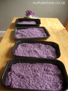 three pans filled with purple rice sitting on top of a wooden table next to a potted plant